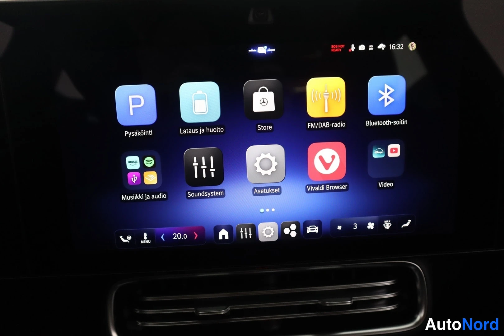 Yksityiskohta: Center console touch screen showing the main menu with app icons for Parking ('Pysäköinti'), Charging/Maintenance ('Lataus ja huolto'), Store, Radio, Bluetooth