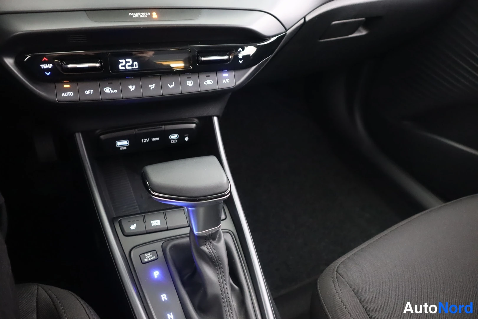 Edestä: Kojelaudan keskusta ja automaattivaihteen valitsin, lämpötilanäytössä 22.0, A/C- ja AUTO-napit sekä USB- ja 12V-liitännät näkyvissä.