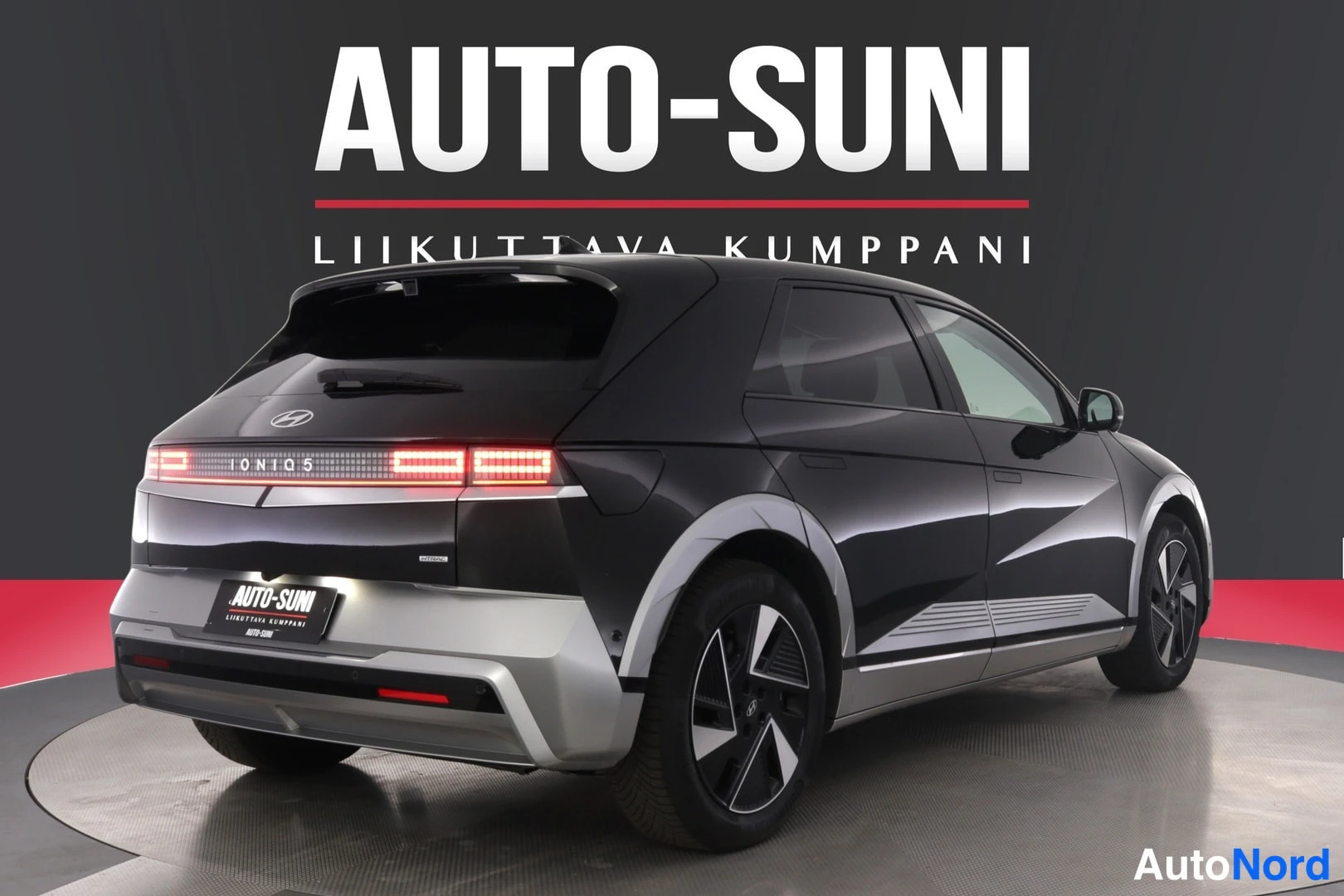 Takaviisto: Musta Hyundai IONIQ 5 -henkilöauto takaa vasemmalta kuvattuna Näyttelytilassa AUTO-SUNI-logon alla.