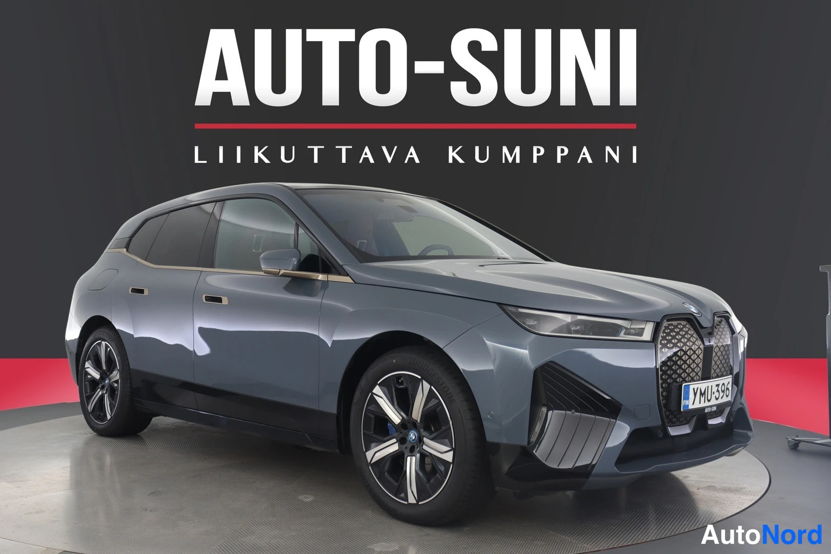 Etuviisto, nokka oikealle: BMW iX 2022 autoprojektiilissa, sinertävän harmaa crossover edestä vasemmalta kuvattuna