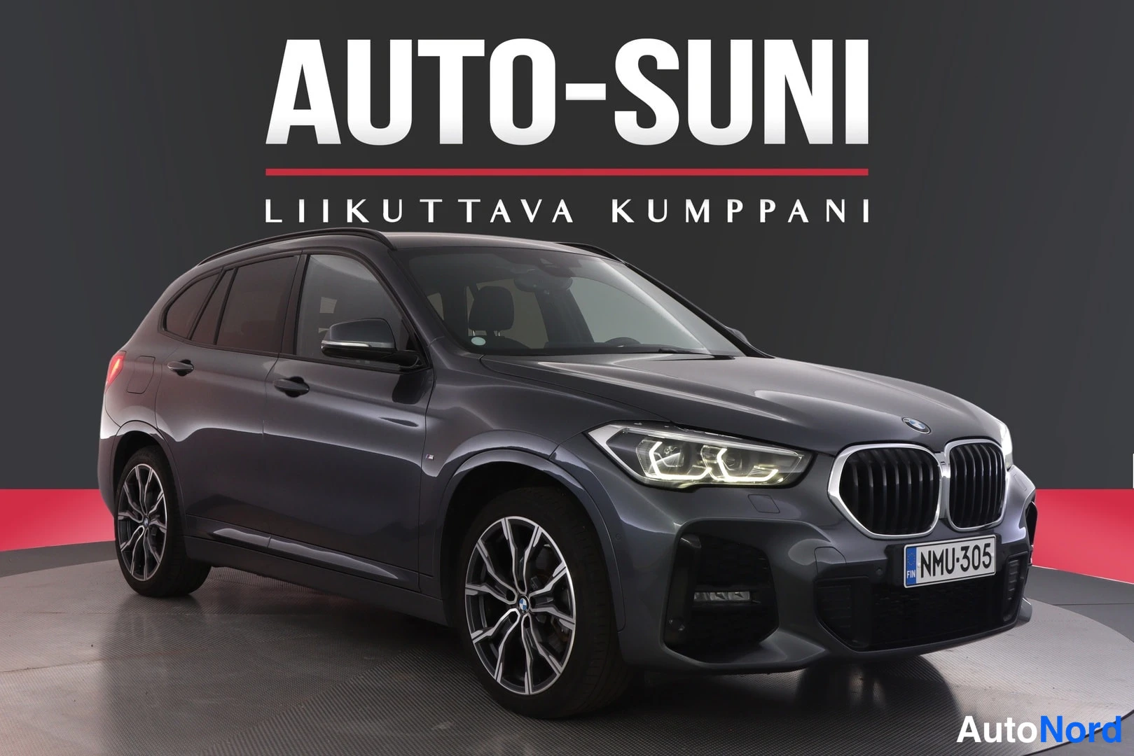 Etuviisto, nokka oikealle: Auton etukulma vasemmalta edestä, tummanharmaa koripinta, BMW-merkkinen farmurityylinen auto myymälätaustaa vasten.