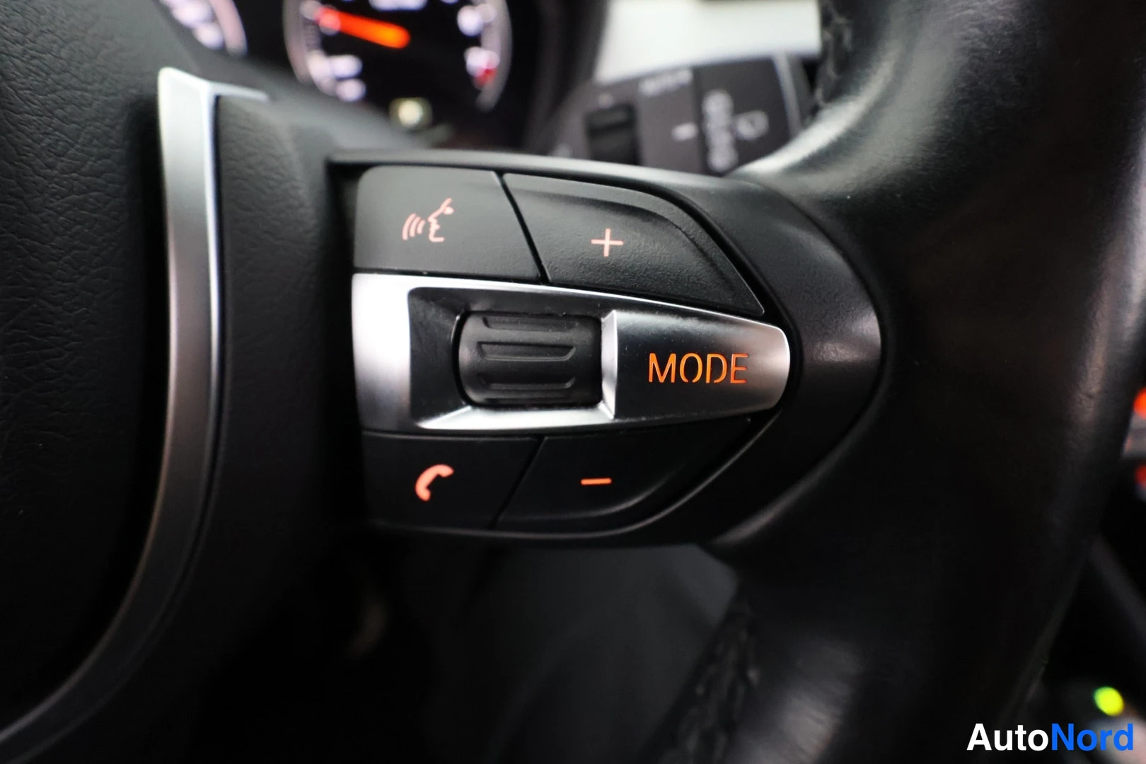 Yksityiskohta: Right steering wheel control buttons showing phone icons, volume controls + and - marked, mode button.