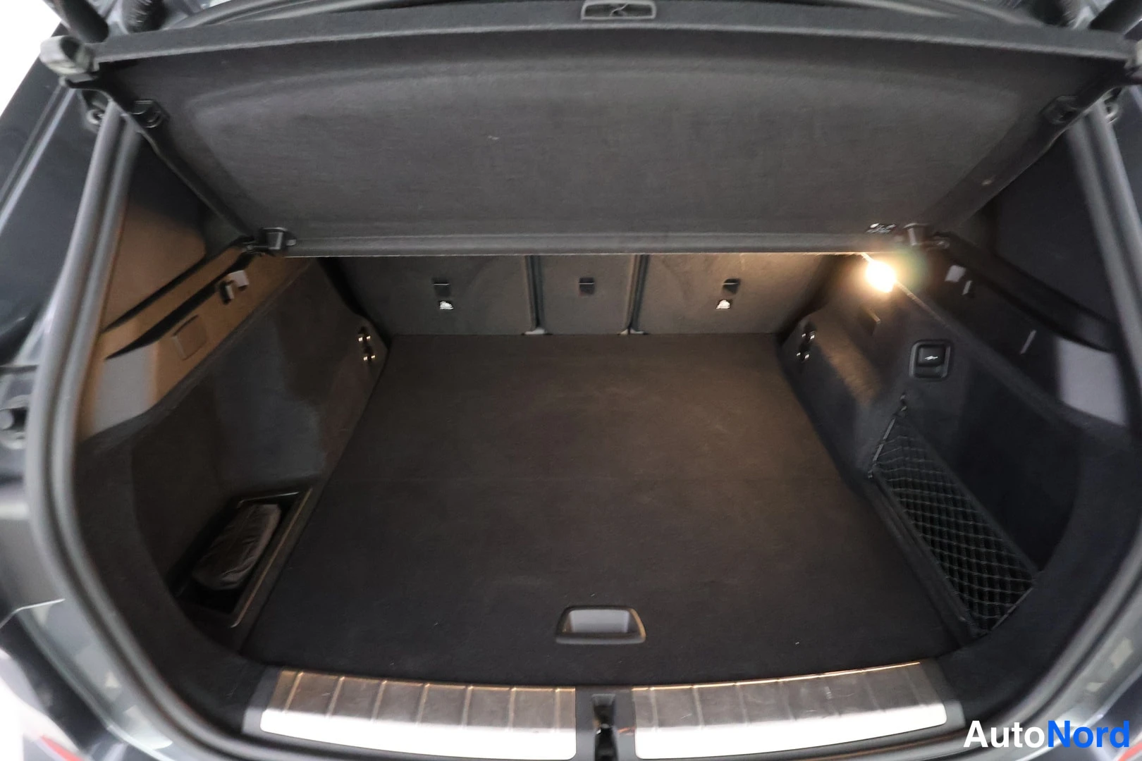 Tavaratila: View into an empty vehicle cargo boot with a retractable tonneau cover stowed at the top. The trunk interior is lined with dark carpeting and features side stor
