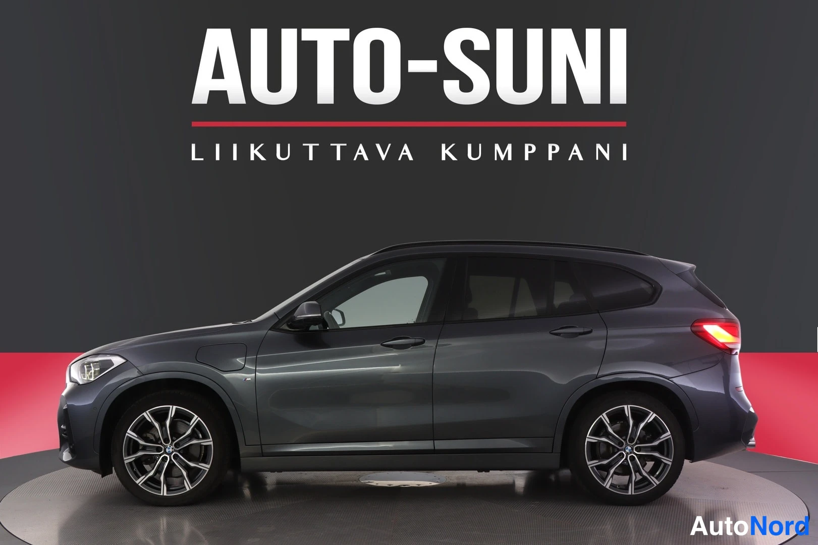 Etuviisto, nokka vasemmalle: Tummanharmaan farmariauton kylki- ja keulaosakuva studiovaalealla taustalla; teksti AUTO-SUNI, Liikuttava kumppani.
