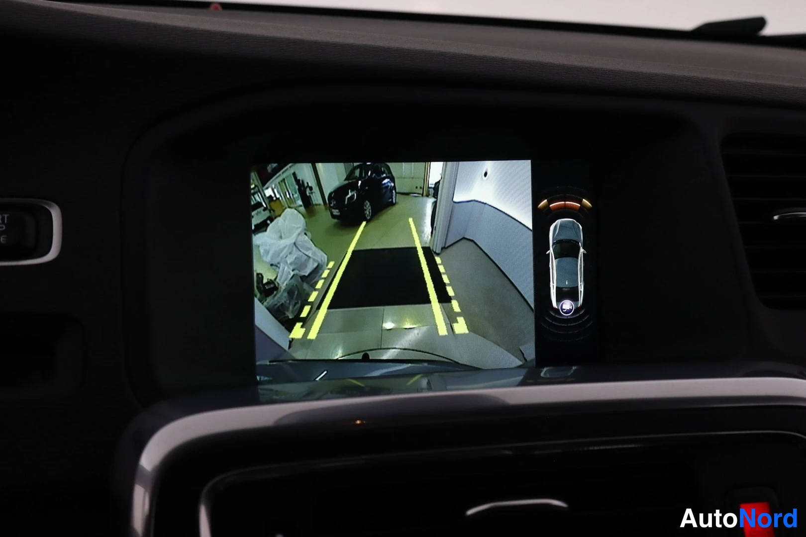Yksityiskohta: Rear camera view on central display showing backup sensor graphics with vehicle positioning aid and parking guidelines