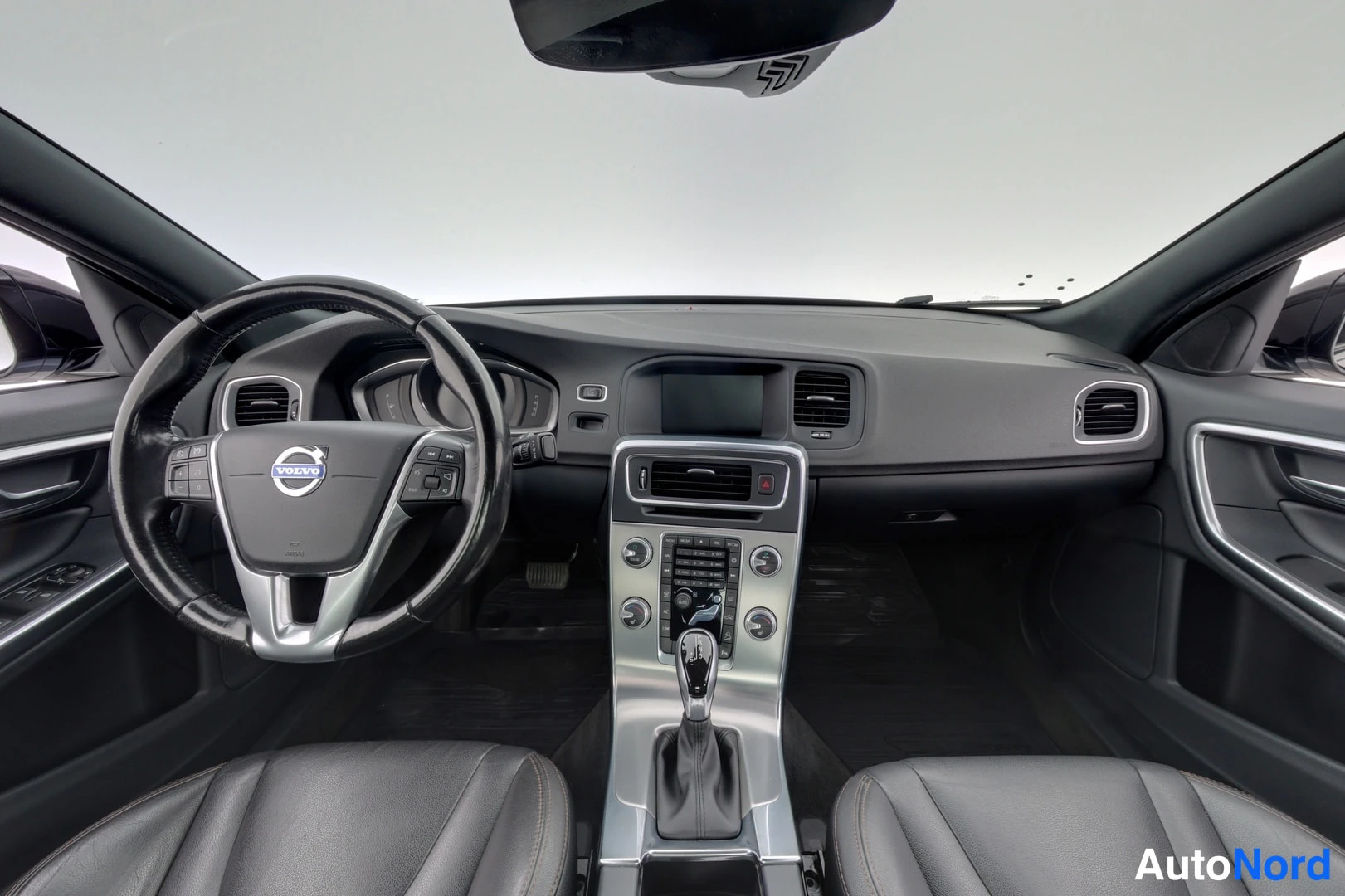 Edestä: Ohjaamo edestä: Volvo-ohjauspyörä, tumma kojelauta, keskinäyttö ja automaattivaihteen valitsin.