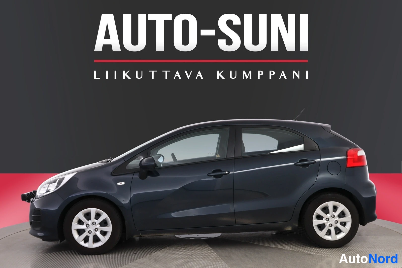 Takaviisto: Tummansininen Kia Rio viistosti takaa vasemmalta kuvattuna, takavalo ja kylki näkyvät.