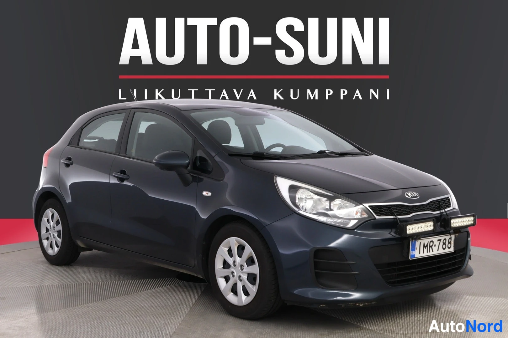 Etuviisto, nokka oikealle: Sinisenharmaa Kia Rio -viistoperä etuosa vasemmalle kuvattuna studioidbindgissä, rekisterillä.