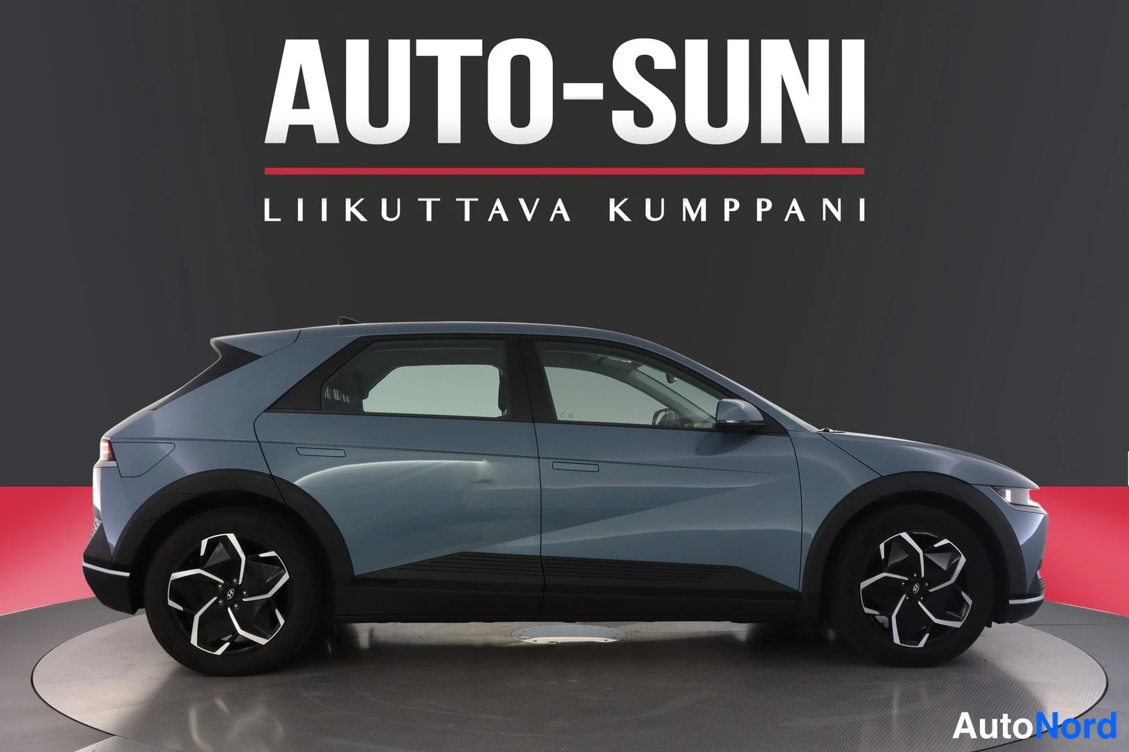 Sivulta: Side profile of the blue car showing five-spoke alloy wheels and door handles flush with the bodywork.