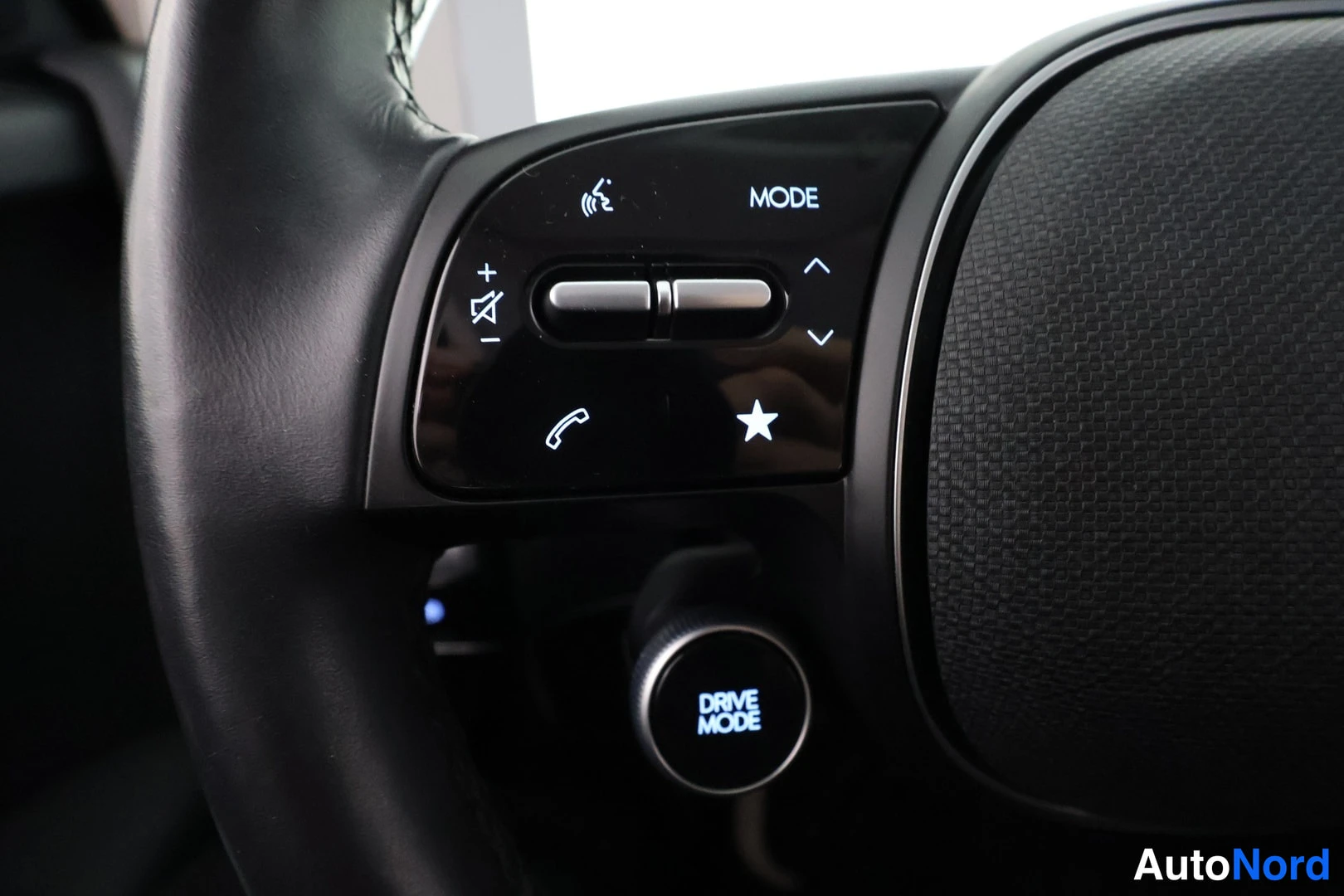 Yksityiskohta: Close-up of the right side of the car's multifunction steering wheel. It features controls for volume (+/-), mute, phone calls, star button, mode selection, and