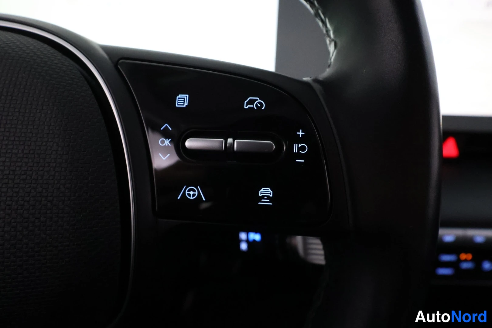 Yksityiskohta: Close-up of the left side of the multifunction steering wheel featuring buttons for cruise control (+/-), lane assist (car between lines icon), collision warnin