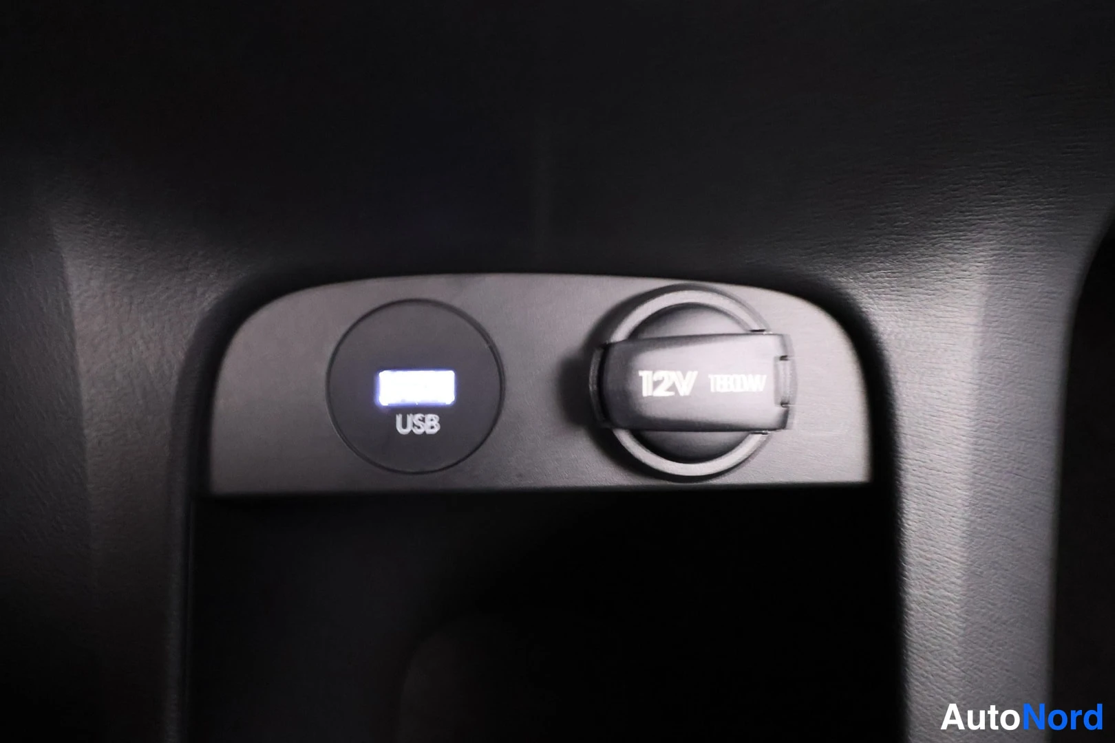Yksityiskohta: Tummassa sisäpaneelissa valaistu USB-portti ja käännettävällä suojakannella varustettu 12V 180W -pistorasia.