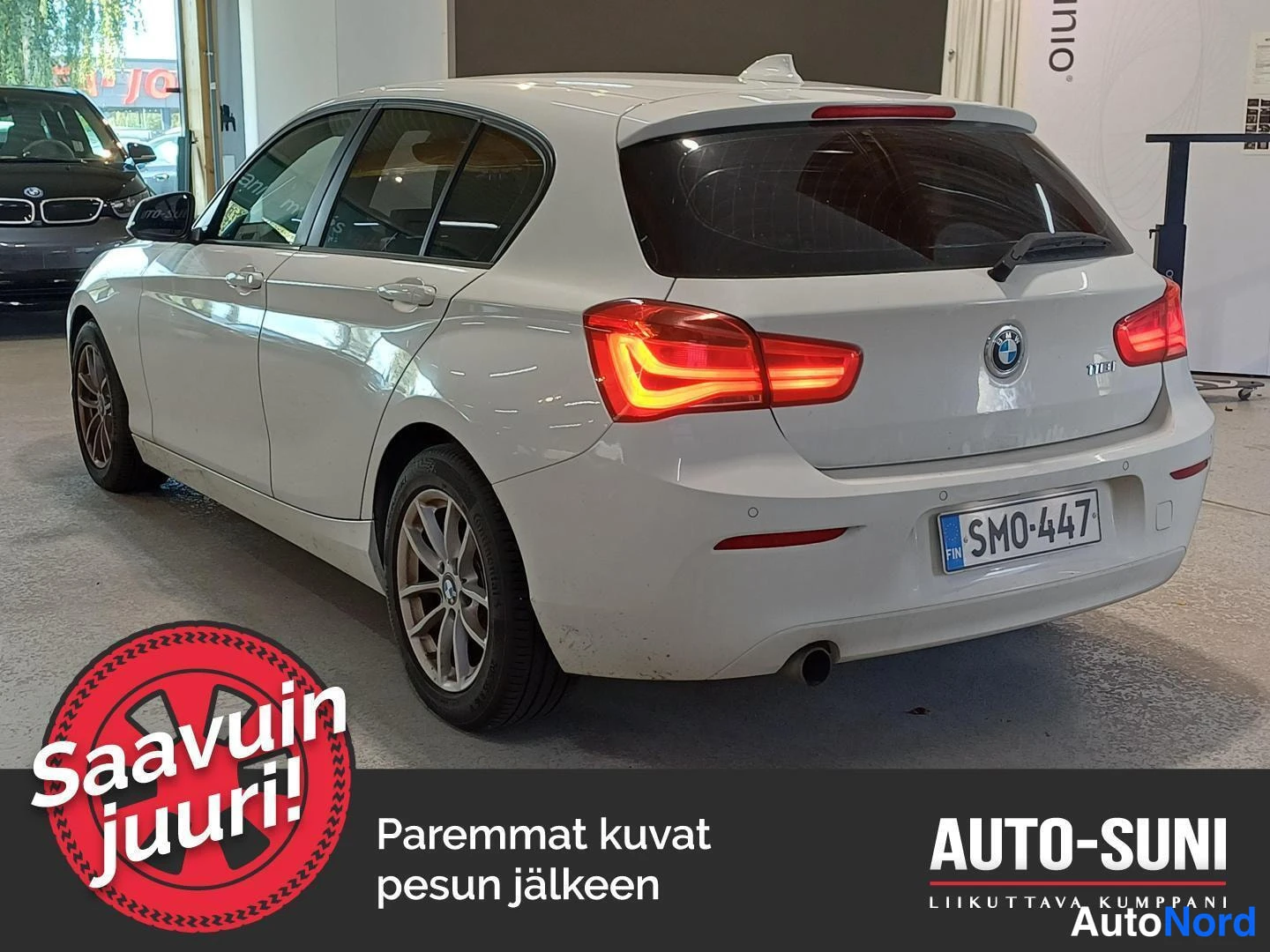 Takaviisto: Takakulma valkoista autoa: punaiset taivalvaloasemat päällä, tavaratilassa oleva lippu ja yksittäinen pakoletku.