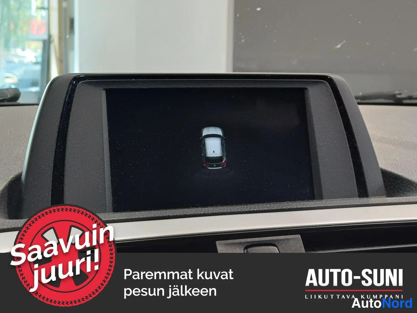 Ohjaamo: Auton keskityksessä oleva näyttö esittää takaparkkaiskameran valmiusnäkymän, jossa on auto ja sen ympärillä olevat parkkeerauspisteet. Näyttö on upotettu kojela