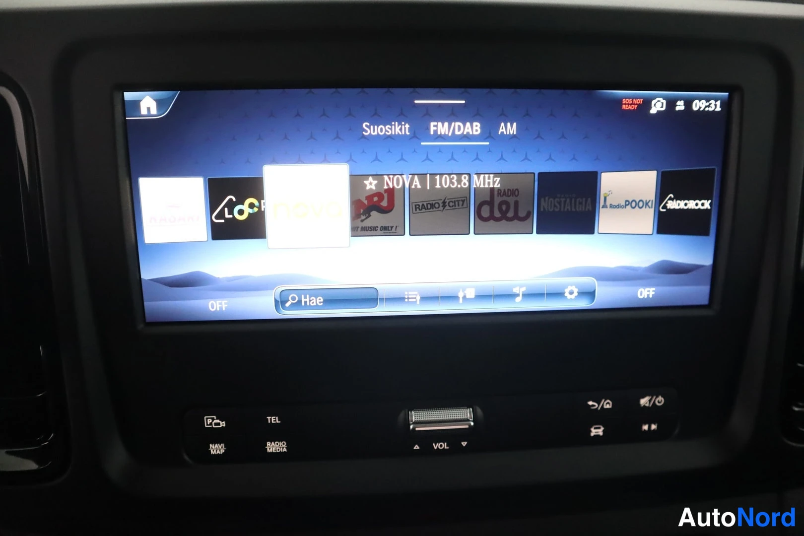 Yksityiskohta: Close-up of the car's infotainment screen displaying FM radio presets. Icons for Mercedes-Benz Radio and various stations like Nova, NRJ, City7, Radio DeL, Nost