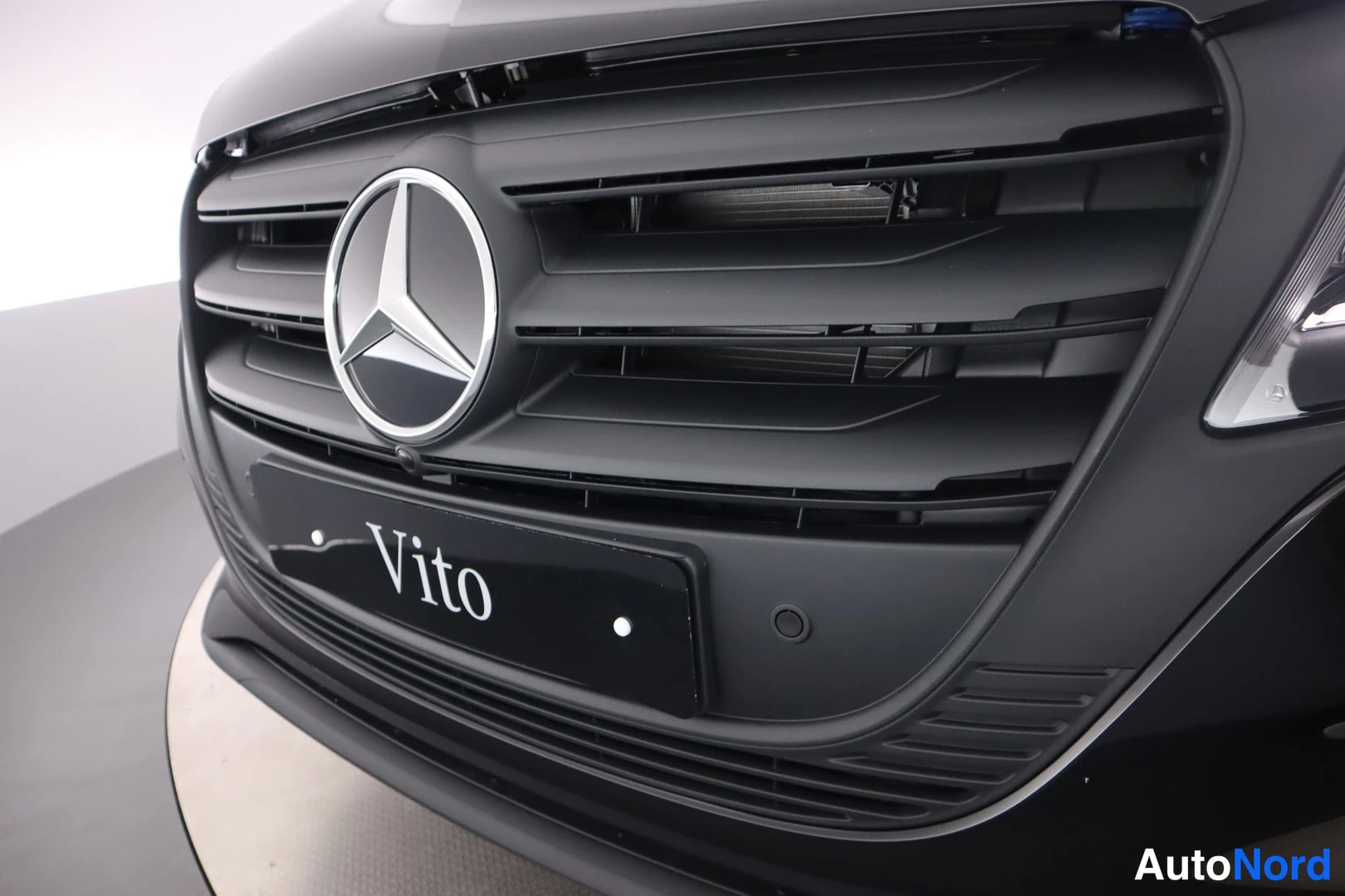 Edestä: Mustan Mercedes-Benz Vito -pakettiauton etusäleikkö lähikuvassa, Mercedes-tähtimerkki keskellä ja Vito-teksti rekisterikilven paikalla.