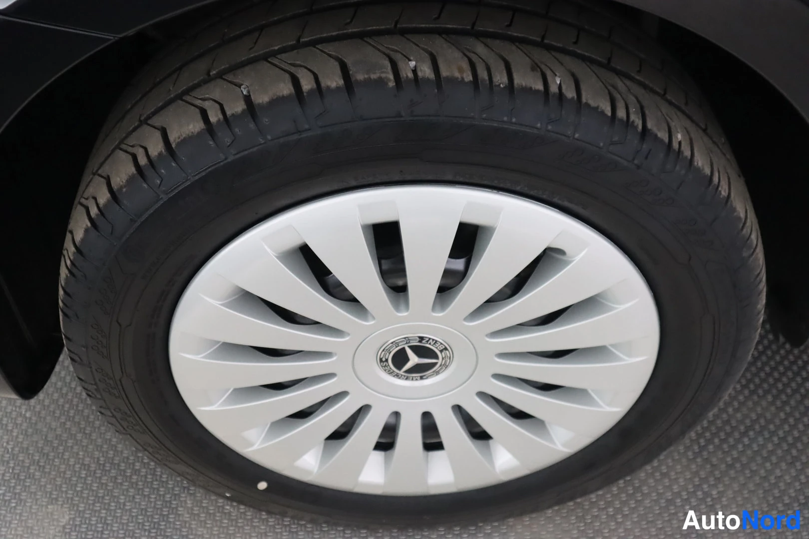 Yksityiskohta: Mustan auton pyörä lähikuvassa, hopeinen Mercedes-Benz-koristekeilakansi keskellä.