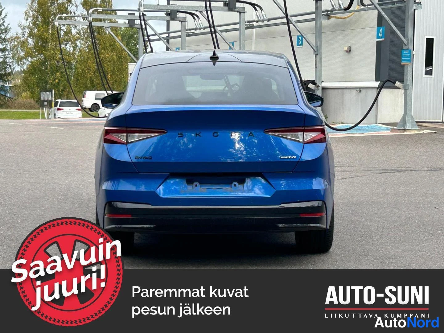 Takaa: Perkuva samasta kirkansinisestä Škoda Enyaqsta latauspisteellä, taaempi logo ja malli kirjoitus selkeästi näkyvissä.