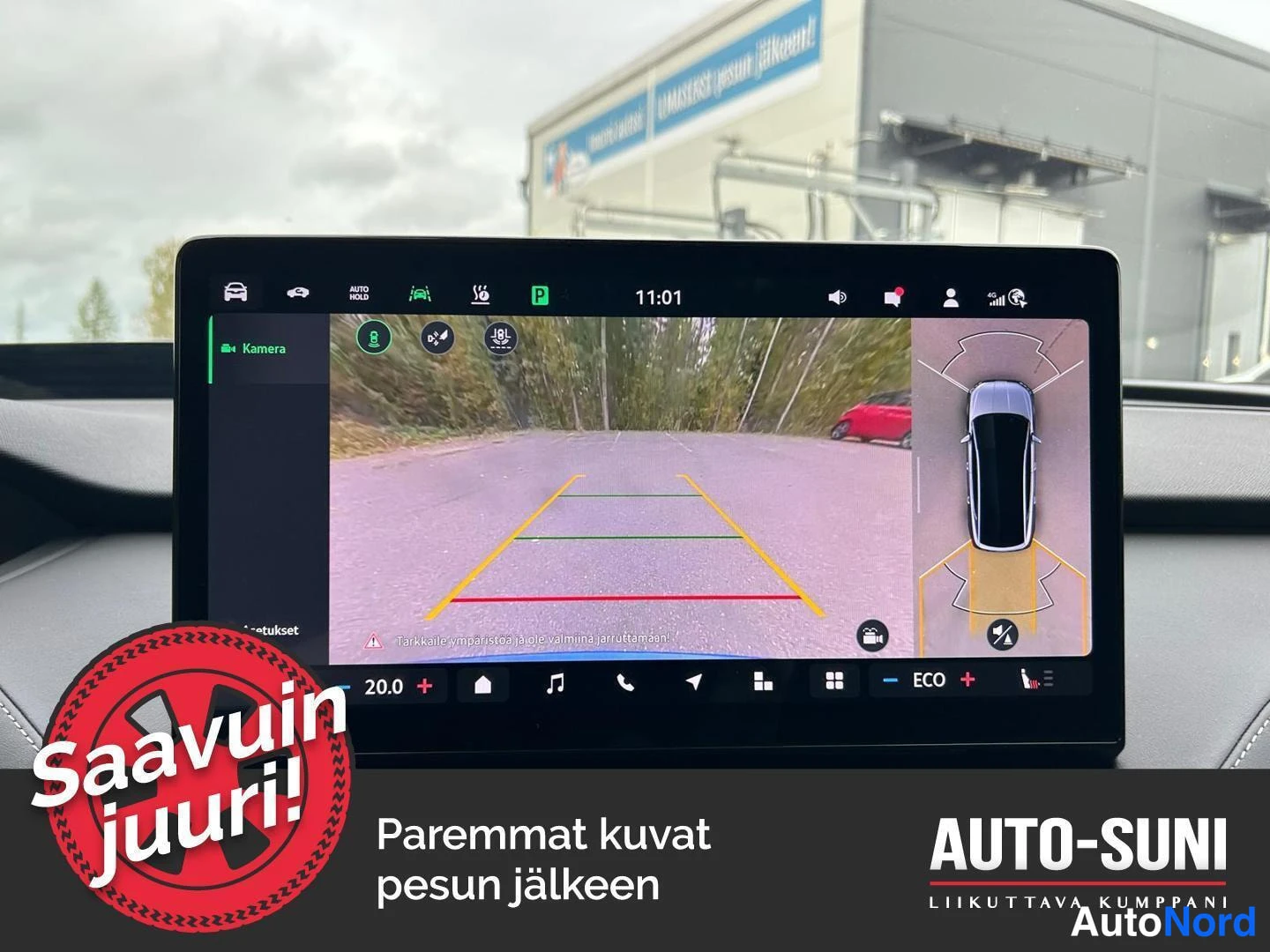 Ohjaamo: Center console display showing a rear-view camera feed with dynamic guidelines. The top part of the screen displays various system icons including parking assis