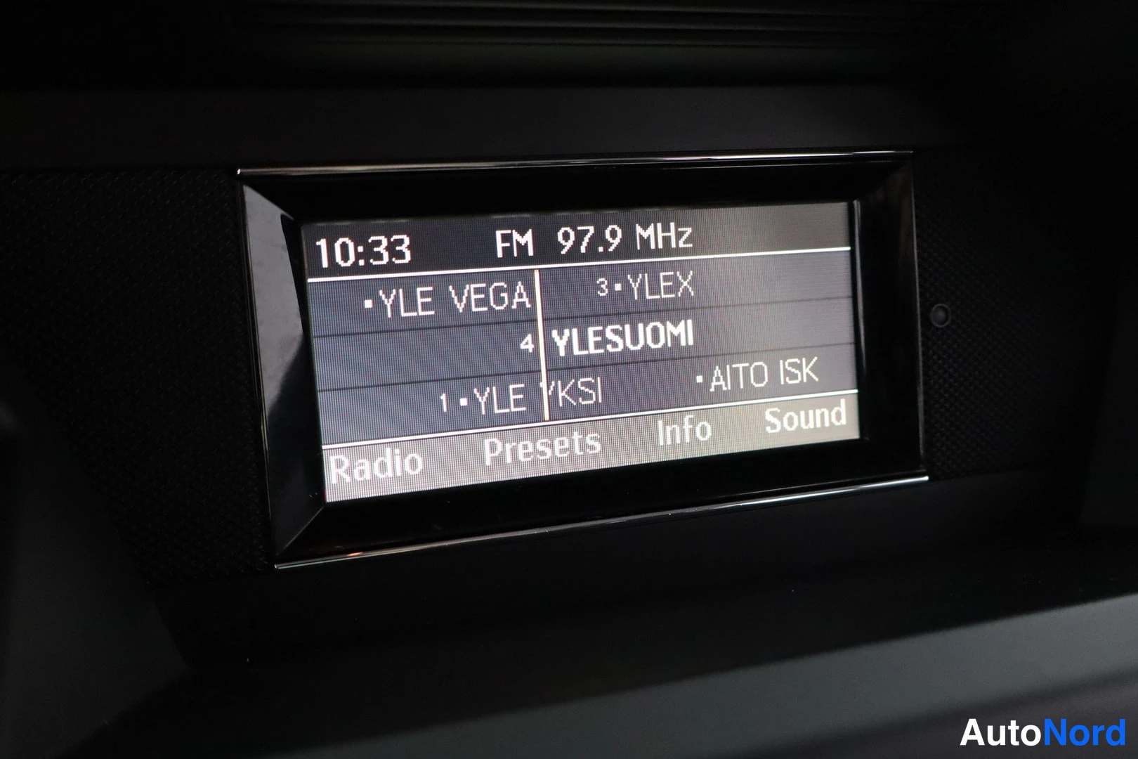 Ohjaamo: Infotainment display screen showing FM radio tuned to frequency 97.9 MHz with visible station presets YLE VEGA, YLEX, YLESUOMI, YLE KSI, and AITO ISK.