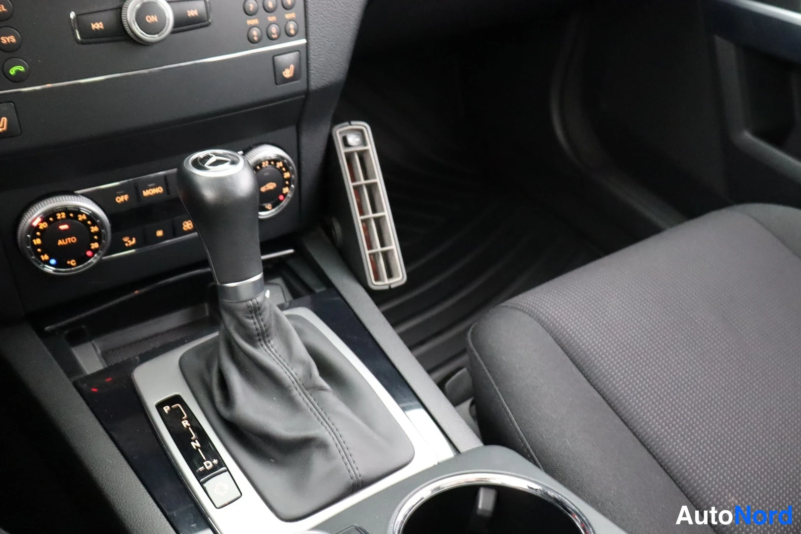 Ohjaamo: Center console area focusing on an automatic transmission gear selector knob featuring a Mercedes-Benz logo.