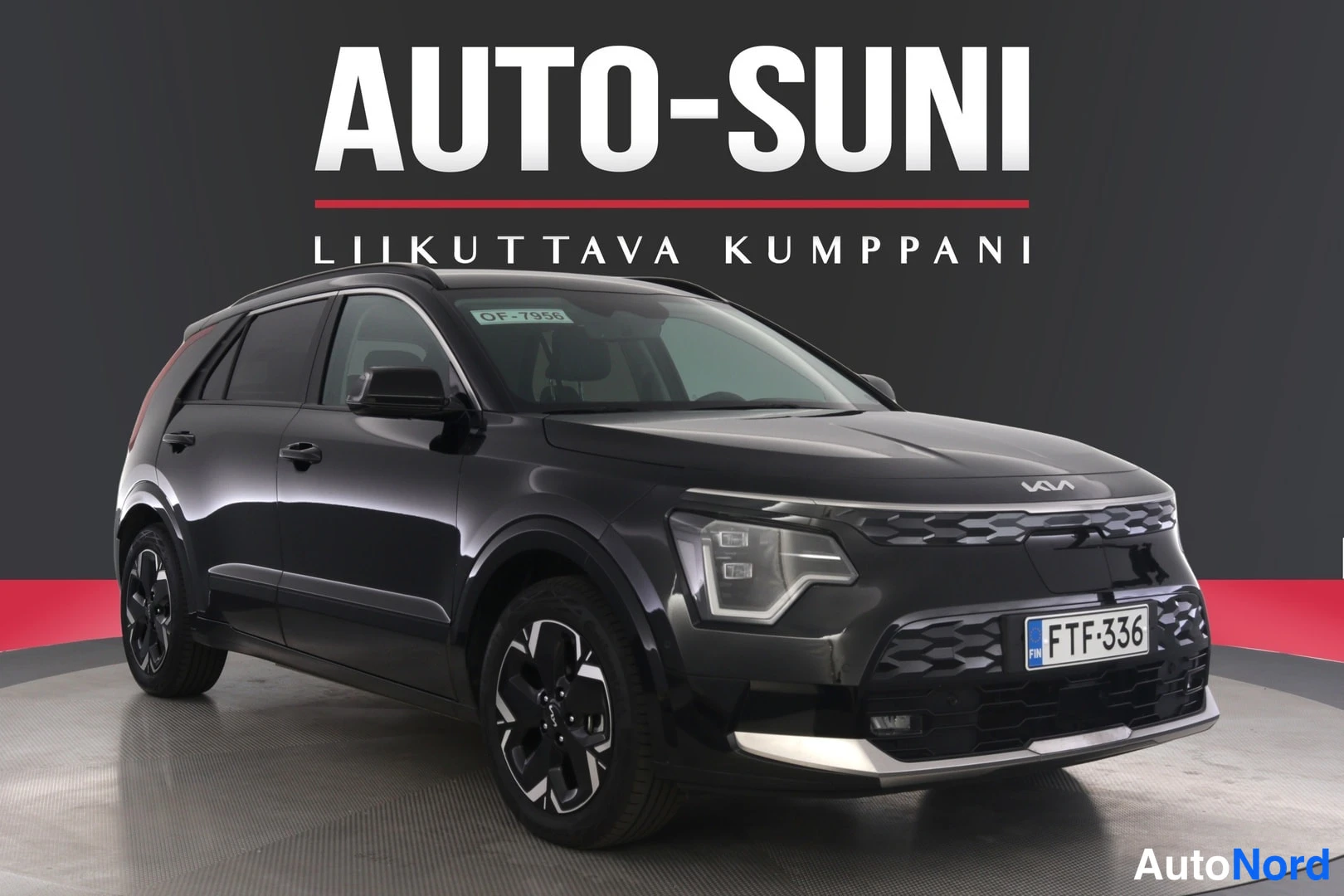 Etuviisto, nokka oikealle: Musta Kia Niro kuvattuna vinosti edestä, keula kuvan oikeassa reunassa, rekisteritunnus.