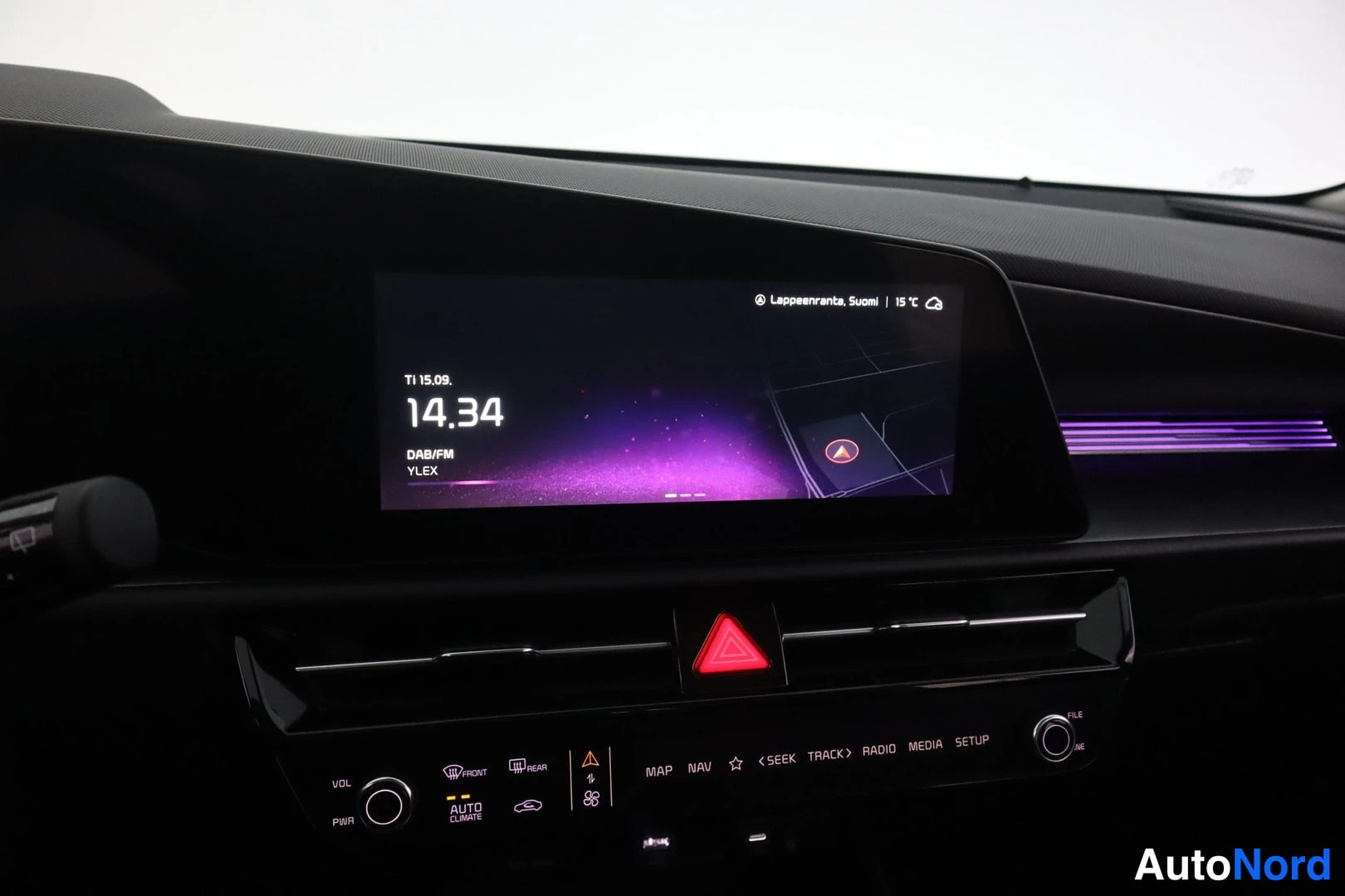 Muu: Infotainment-näytön kotivalikko: DAB/FM-radio YLEX, kello 14.34 ja säätiedot Lappeenrannassa; kojelaudassa violettia tunnelmavalaistusta.
