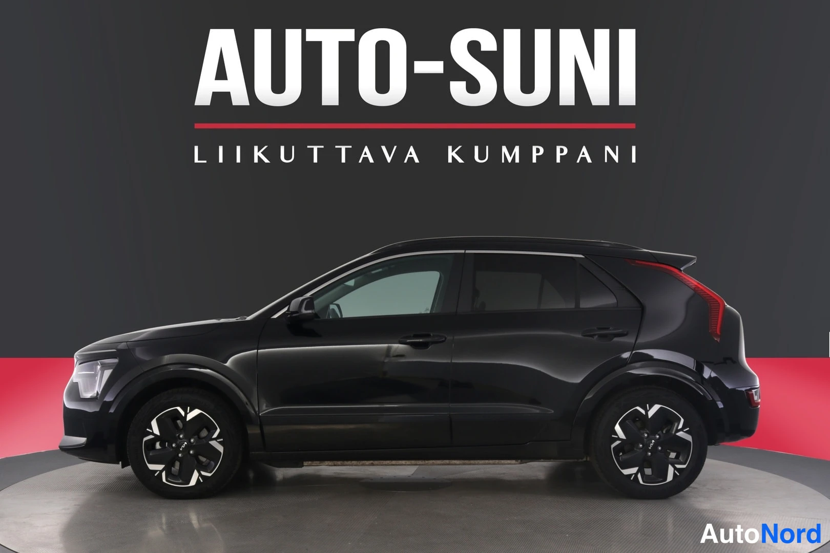 Sivulta: Musta Kia-korkeatason automobiili näkyy tässä profiilikuvassa. Auto on musta ja se seisoo punaisella ja harmaalla taustalla. Kuvassa näkyvät vain auton kyljet.