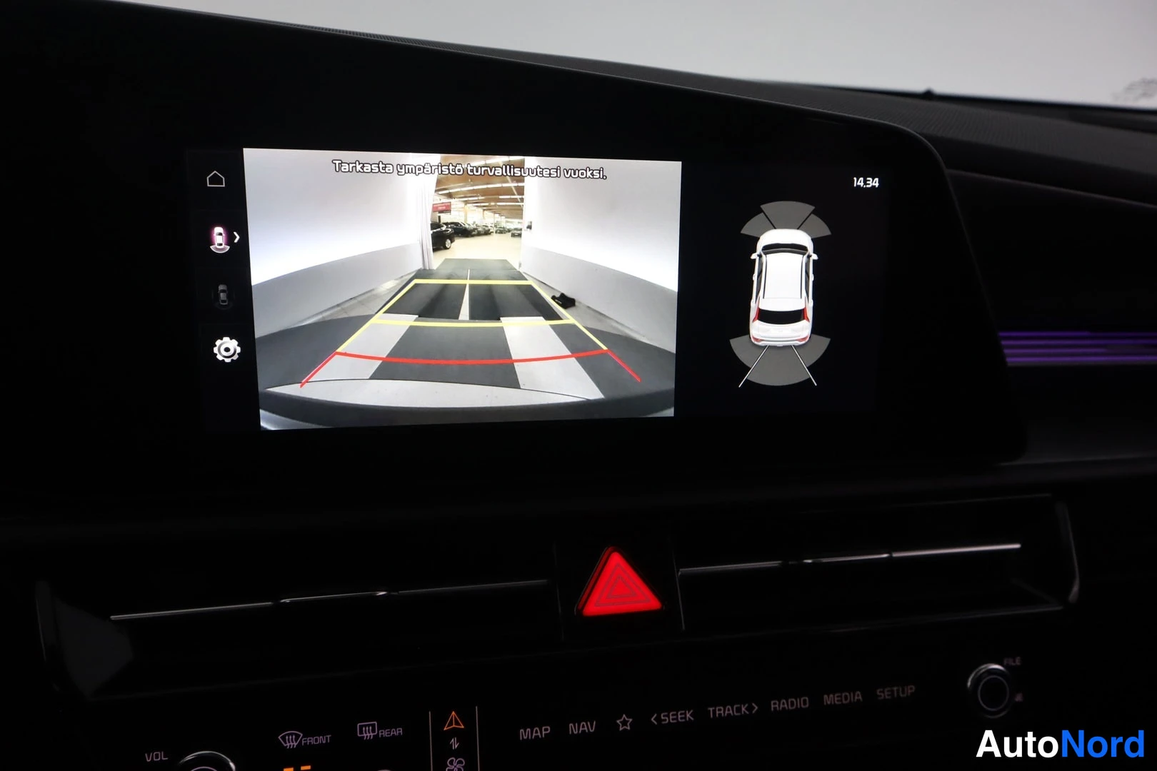 Muu: Infotainment-näytöllä ympäristökameran kuva ohjausviivoineen, ajoneuvon ympäränäkymägraafiikka ja teksti 'Tarkasta ympäristö turvallisuutesi vuoksi.'