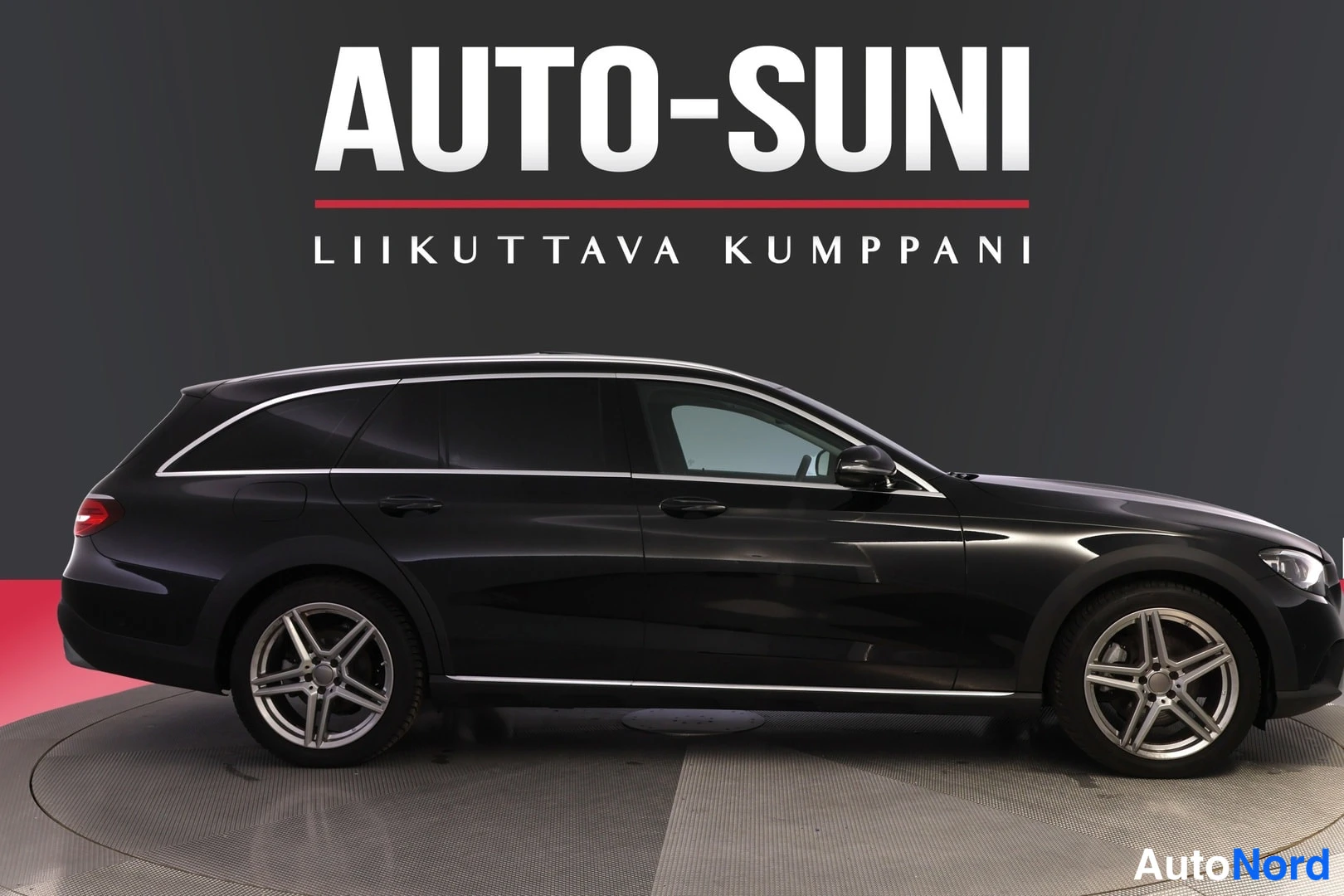 Sivulta: Musta farmariauto sivulta kuvattuna studiotaustassa, hopeiset vanteet, AUTO-SUNI-kyltti taustalla.
