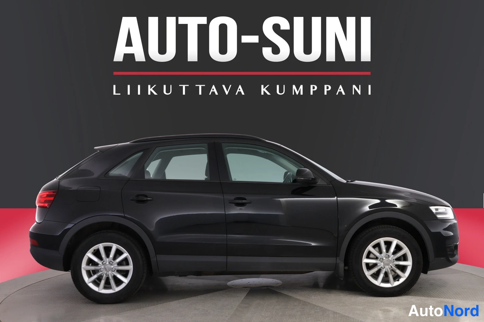 Sivulta: Musta Audi Q3 -maast_auto etuosoalta oikeaan alakulmaan kääntyneenä studiotaustaa vasten, rekisteritunnus, valkoiset vanteet ja AUTO-SUNI mainosteksti taustalla