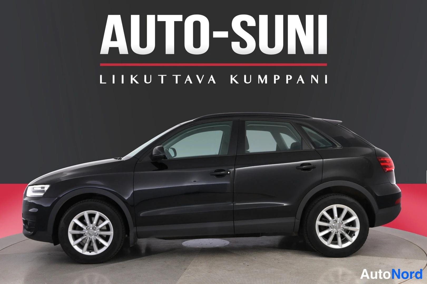 Etuviisto, nokka vasemmalle: Auton sivu- ja keulakuva: musta Audi Q3 -henkilöauto studio-/näyttelytaustassa, AUTO-SUNI-mainosteksti kuvan yläosassa.