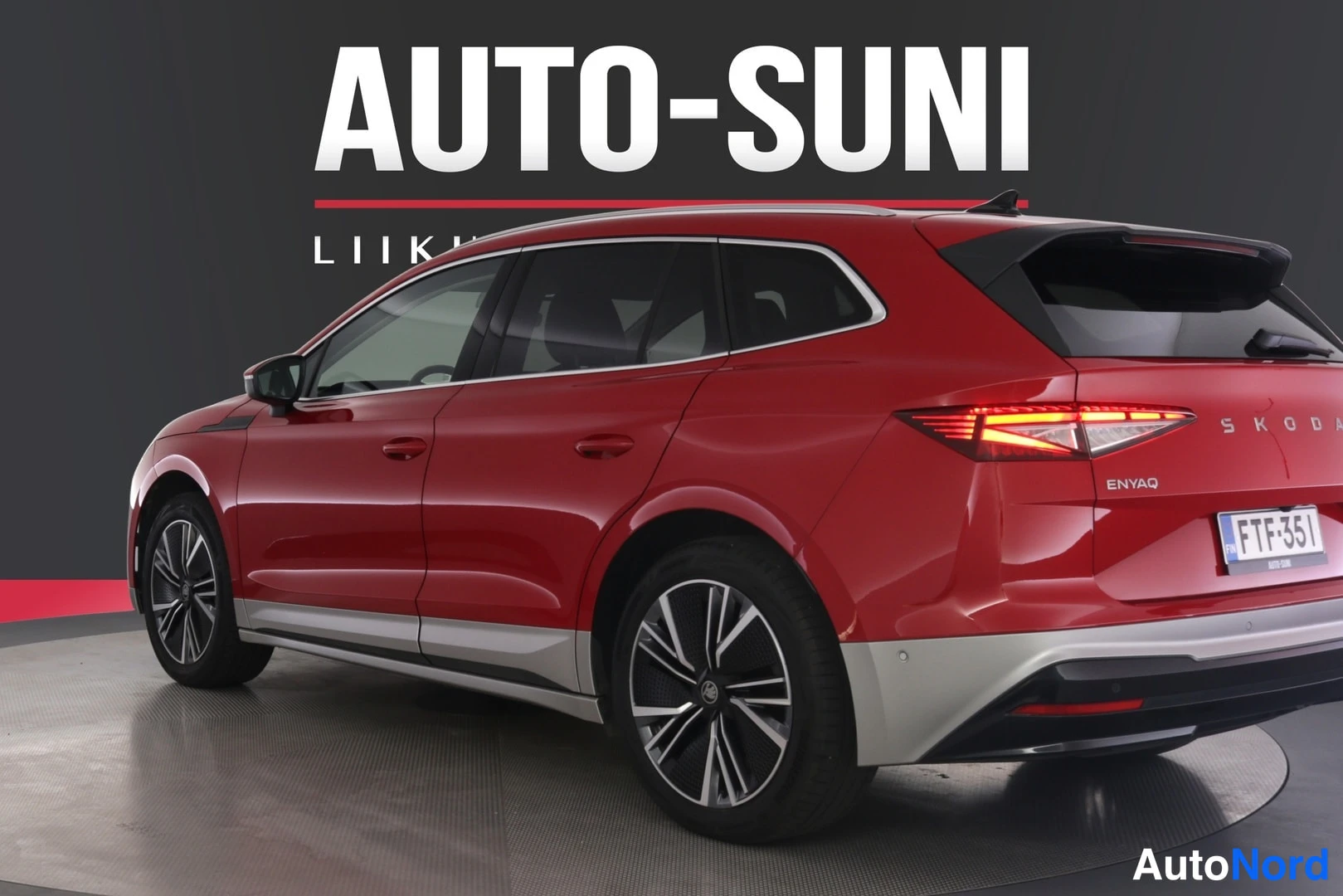 Takaviisto: Punaisen Skoda Enyaqn takaosa kolmannesnäkymästä oikealta taaksepäin, SKODA- ja ENYAQ-tekstit takaluukussa, rekisterikilpi, tummat ikkunat ja kevytmetallivantee