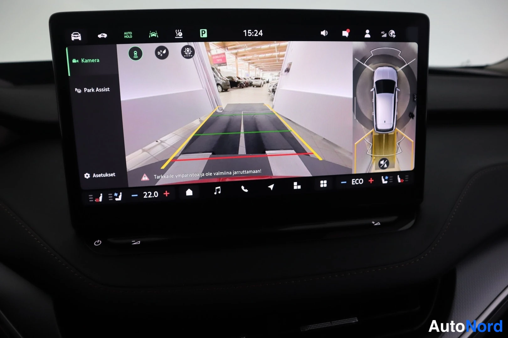Yksityiskohta: Keskikonsolin kosketusnäyttö näyttää peruutuskameran kuvan ja Park Assist -näkymän, teksti 'Tarkkaile ympäristöä ja ole valmiina jarruttamaan!'