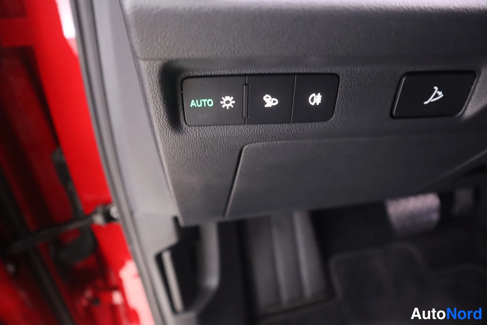 Yksityiskohta: Autovalot-katkaisijan ryhmä, jossa AUTO-toiminto, sumuvalot ja kauko-/ lähivalot -painikkeet punaisen auton etumuovipaneeleissa.