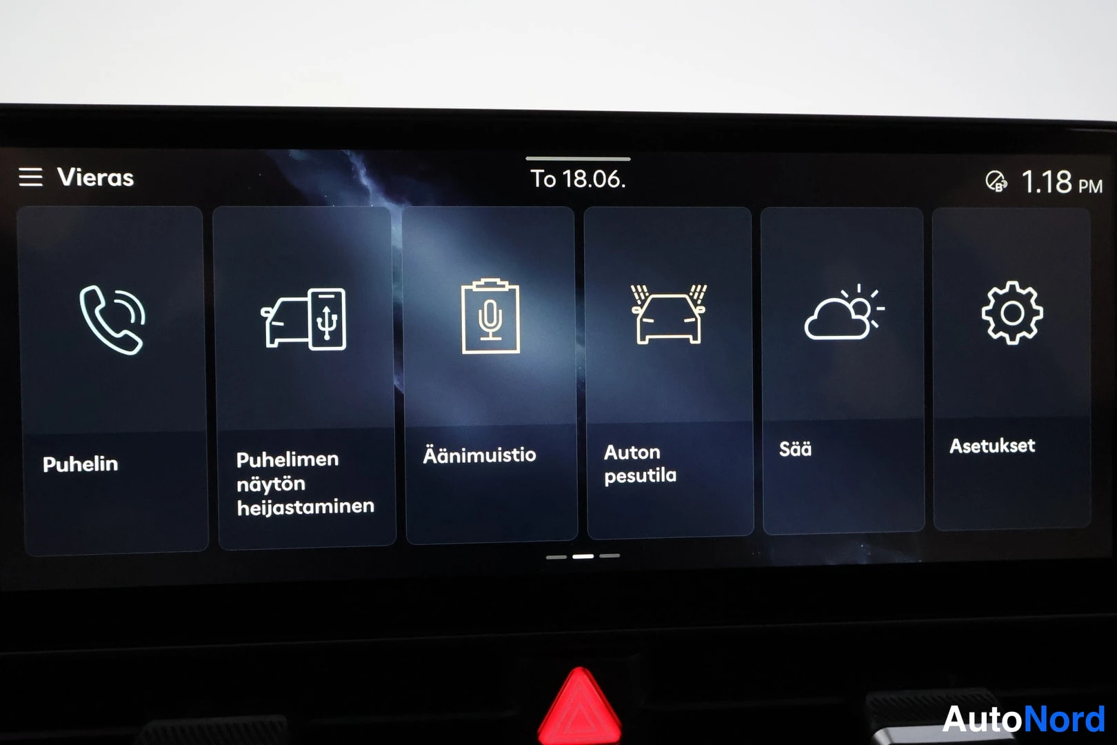 Yksityiskohta: Autoon sisätilan infotainment-kosketusnäyttö, jonka valikossa ruutuja teksteinä Puhelin, Puhelimen näytön heijastaminen, Äänimuistio, Auton pesutila, Sää ja Ase