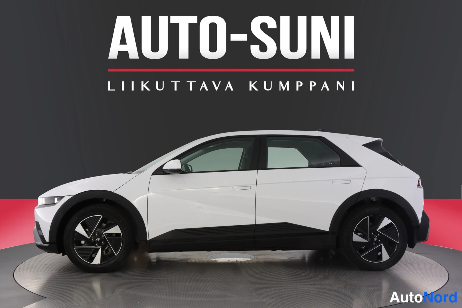 Sivulta: Valkoisen Hyundai IONIQ 5 -auton sivuprofiili näkyvissä studio-vaalealla lavalla, dark tausta ja Auto-Suni-mainosbanneri.