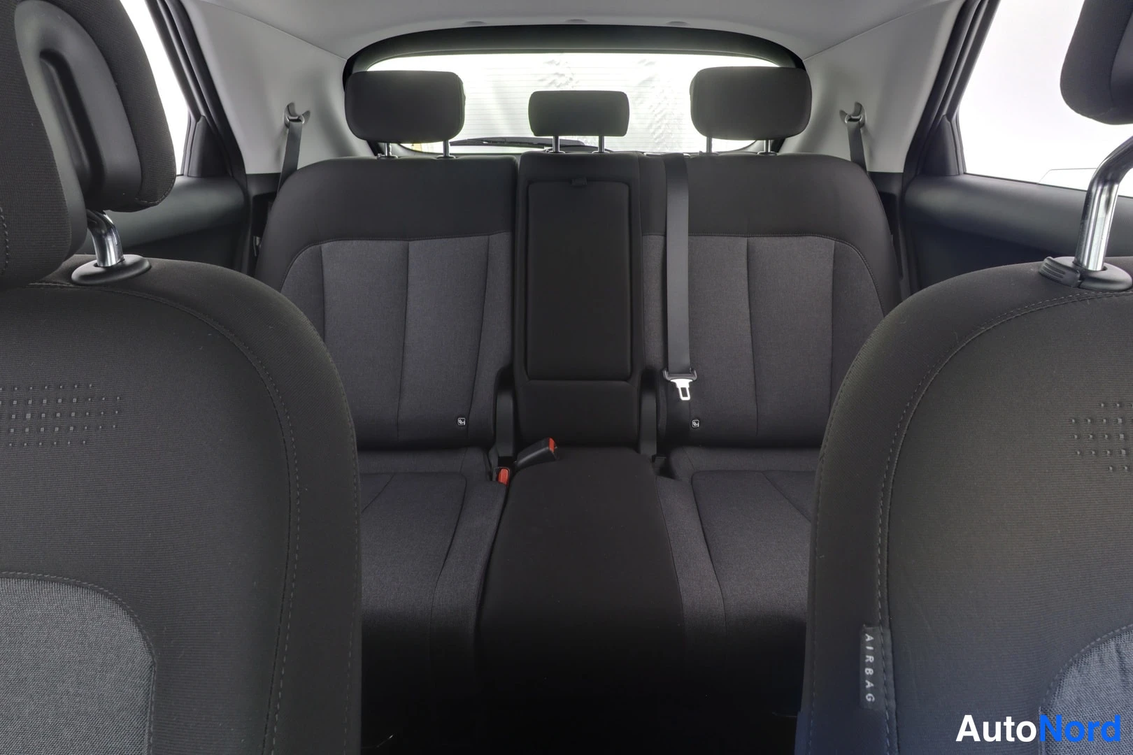 Muu: Hyundai IONIQ 5:n takaistuin kolmella istuimella, tumma tekstiiliverhoilu, keskikonsoli kaatuneena ja kolme niskatukea. Etuistuinten selkänojat AIRBAG-tekstillä