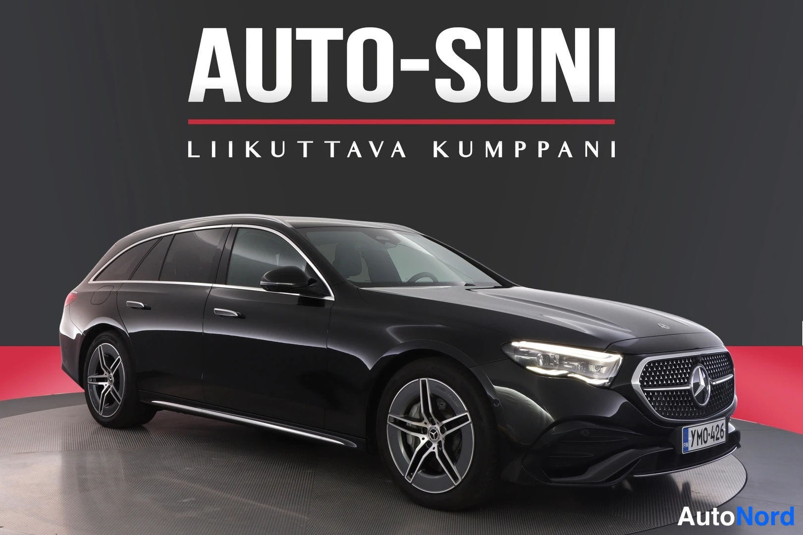 Etuviisto, nokka oikealle: Musta Mercedes-Benz farmariauto myyjän pimeässä studioavustuksessa, keulan ja vasemman sivun näkymä; teksti AUTO-SUNI ylhäällä.