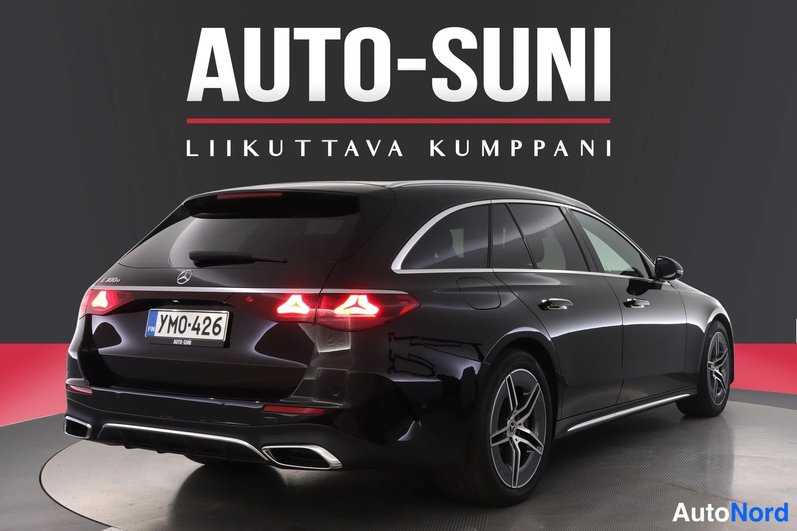 Takaviisto: Mustan Mercedes-Benz farmarin takaosa ja vasen kylki näkyvissä, takavalot päällä, rekisterikilpi.