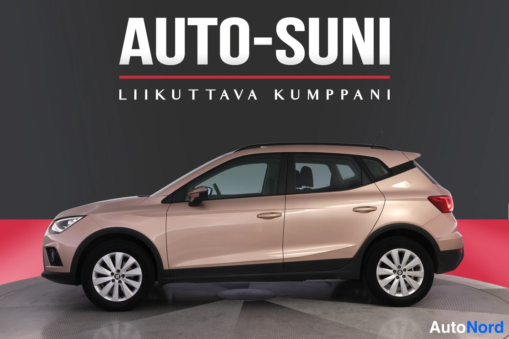 Etuviisto, nokka vasemmalle: Vaaleanpunaisen beigen Seat Arona -henkilöauto sivulta etuviistöstä valkoihoisessa studiossa, tumma tausta mainostekstillä.