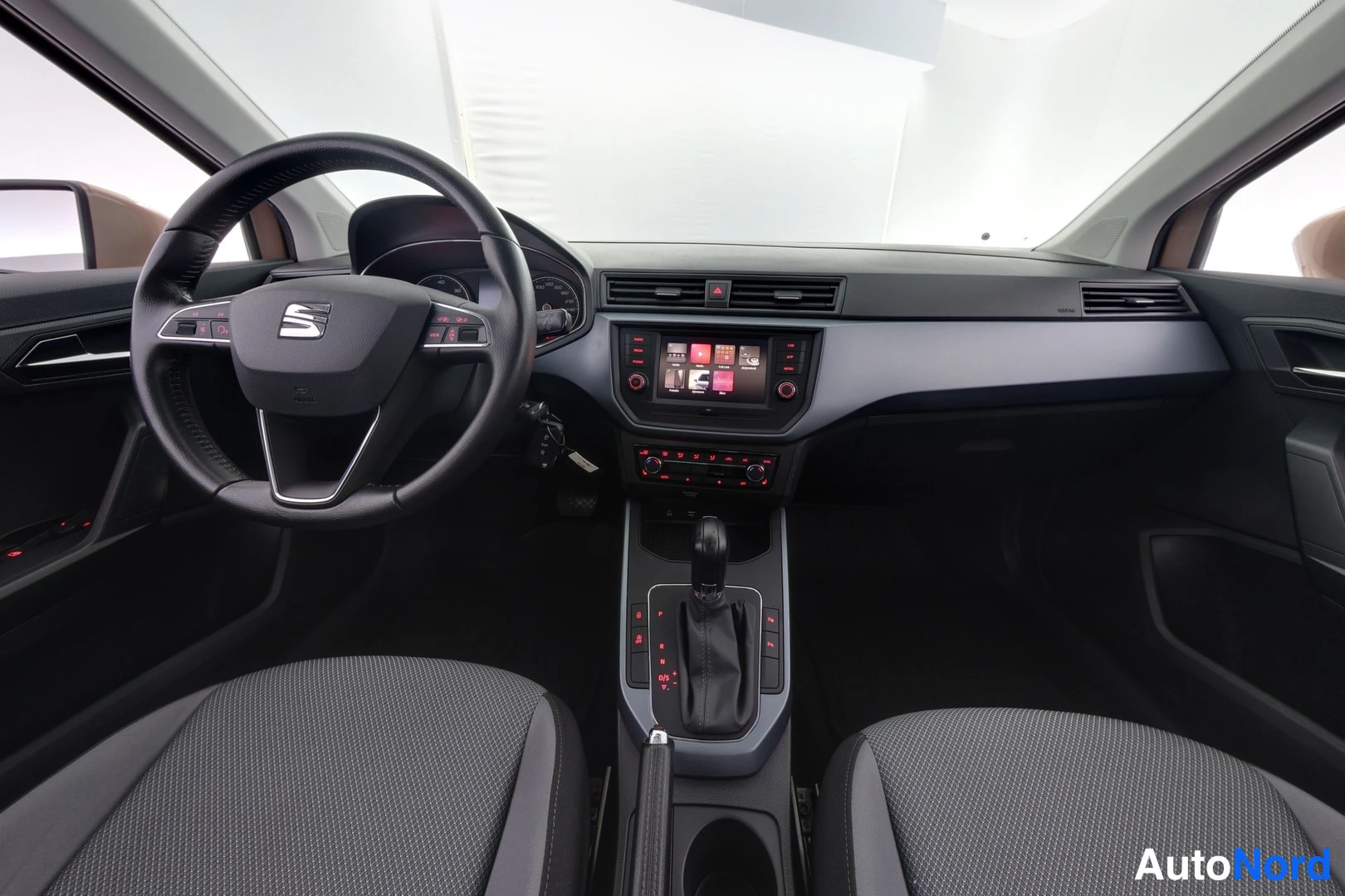 Muu: Seat Aronan ohjaamo etukädestä: ratissa Seat-logo, keskikonsolissa kosketusnäyttö ja automaattivaihteen valitsin, tummat kangasistuimet.