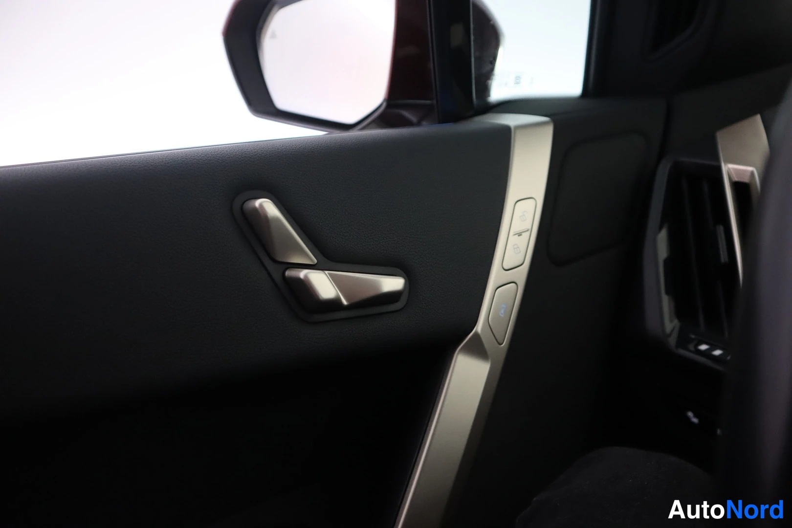 Yksityiskohta: Auton sisätilan lähikuva: oviverhoilu ja seat adjustment -nappiryhmä, takana sivupeili.