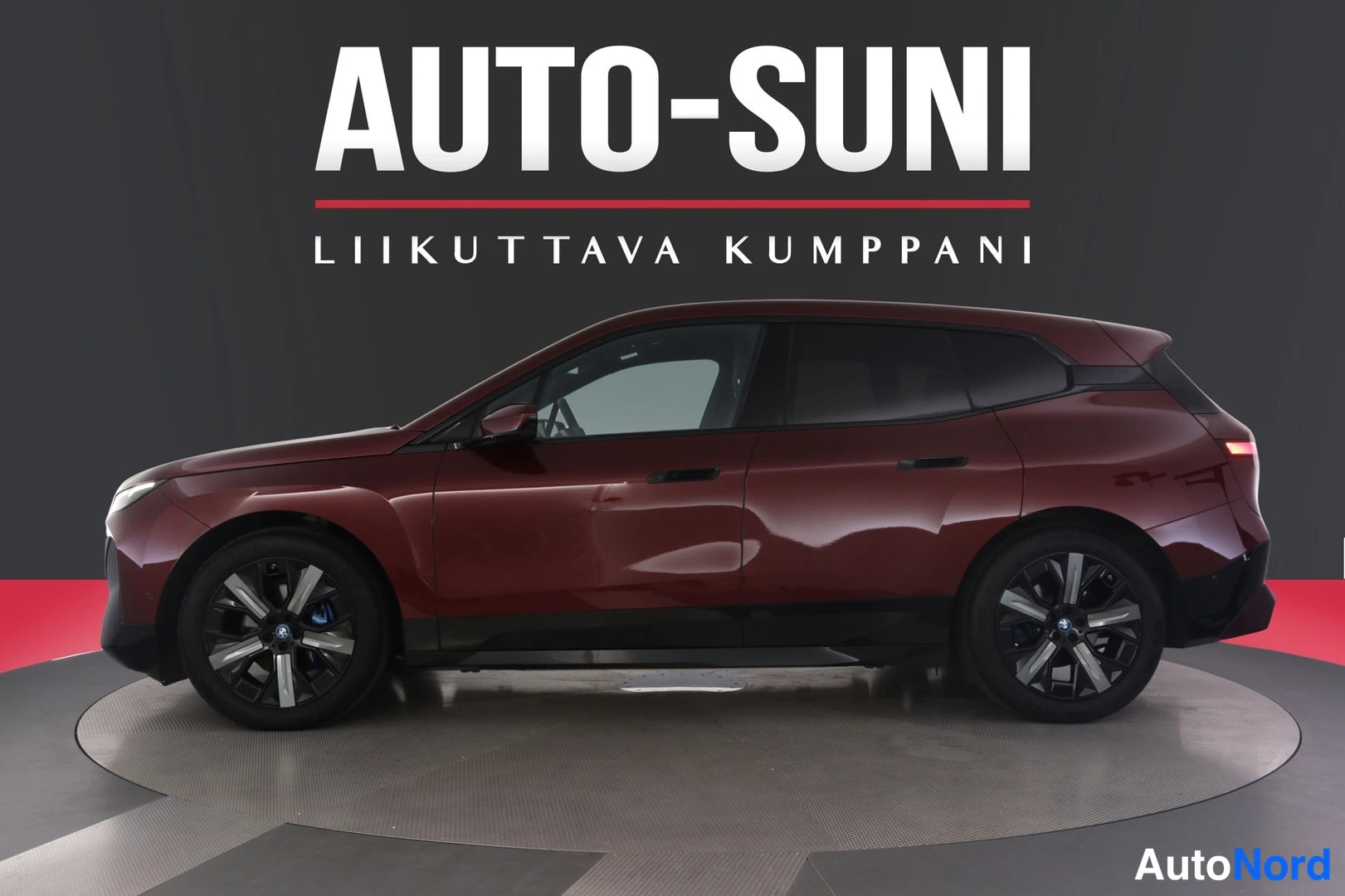 Sivulta: Punainen BMW iX -maasturin sivuprofiili myyjän studio­taustaa vasten.