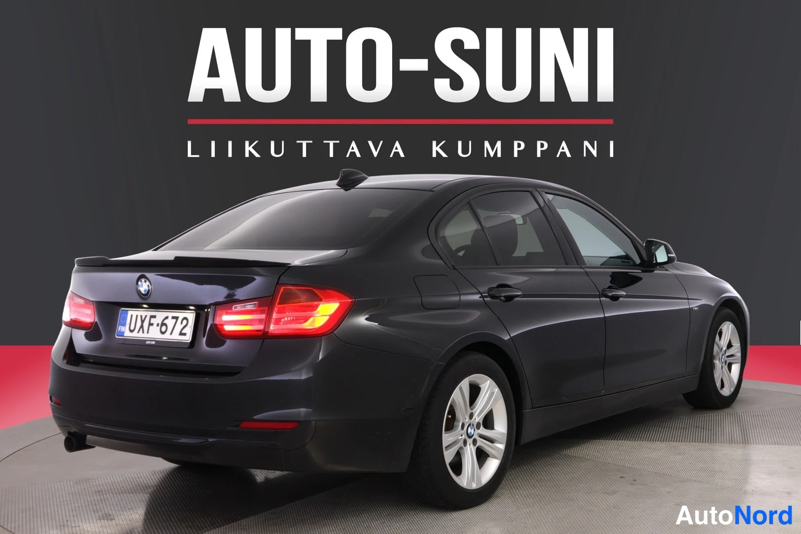 Takaviisto: Musta sedan takakulmasta vasemmalta, rekisterikilpi, tummassa studiossa.