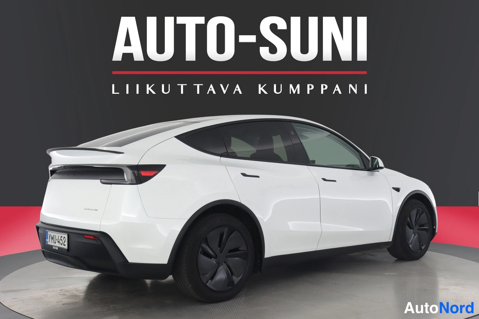Takaviisto: Valkoinen Tesla Model Y takaa kolmesta neljännestä vasemmalta, studion pyörivällä alustalla.