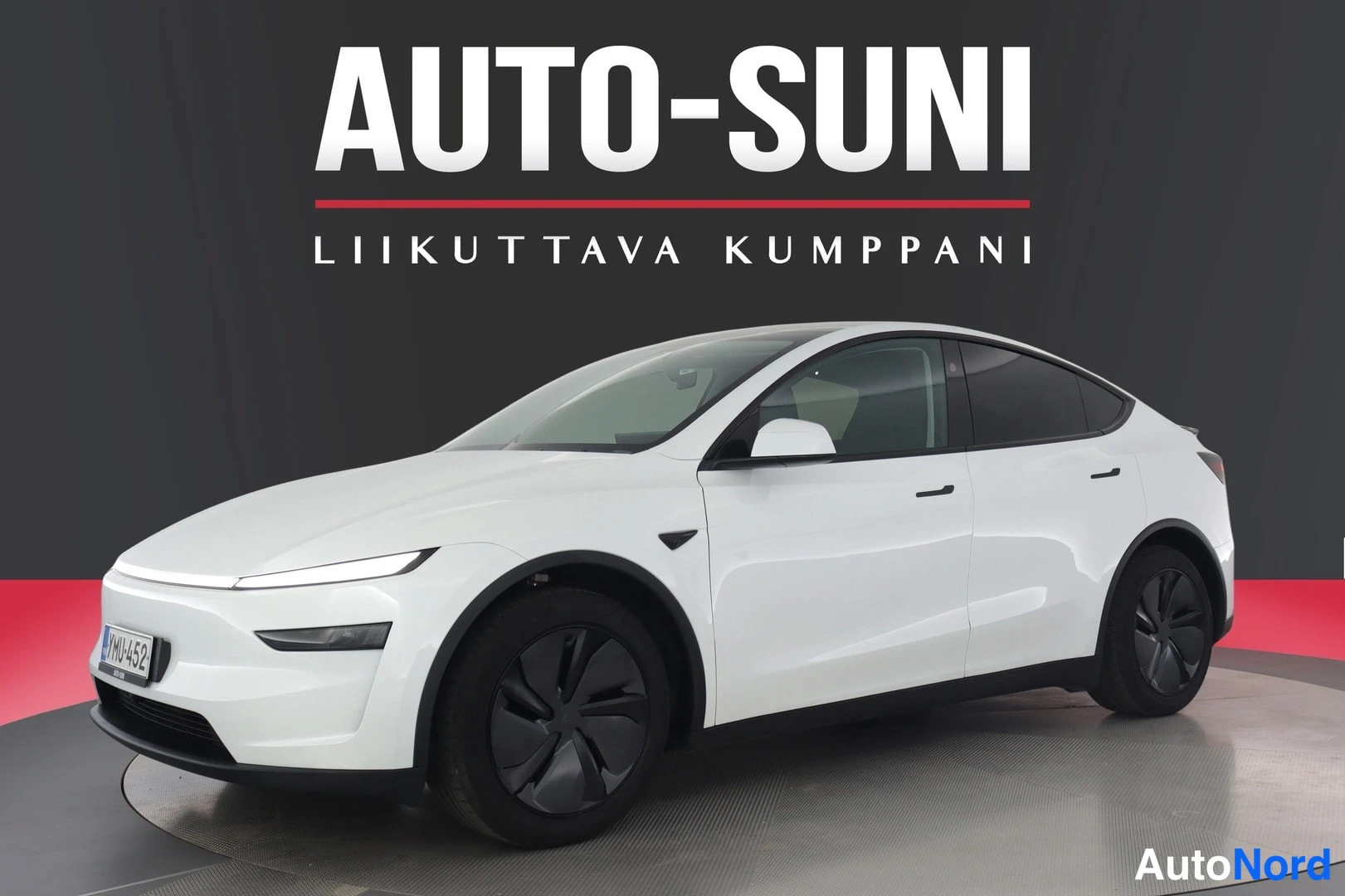 Etuviisto, nokka vasemmalle: Valkoinen Tesla Model Y etuviistosta studiokuvassa, rekisteritunnus YMÜ-452, Auto-Suni-mainoskuvatus.