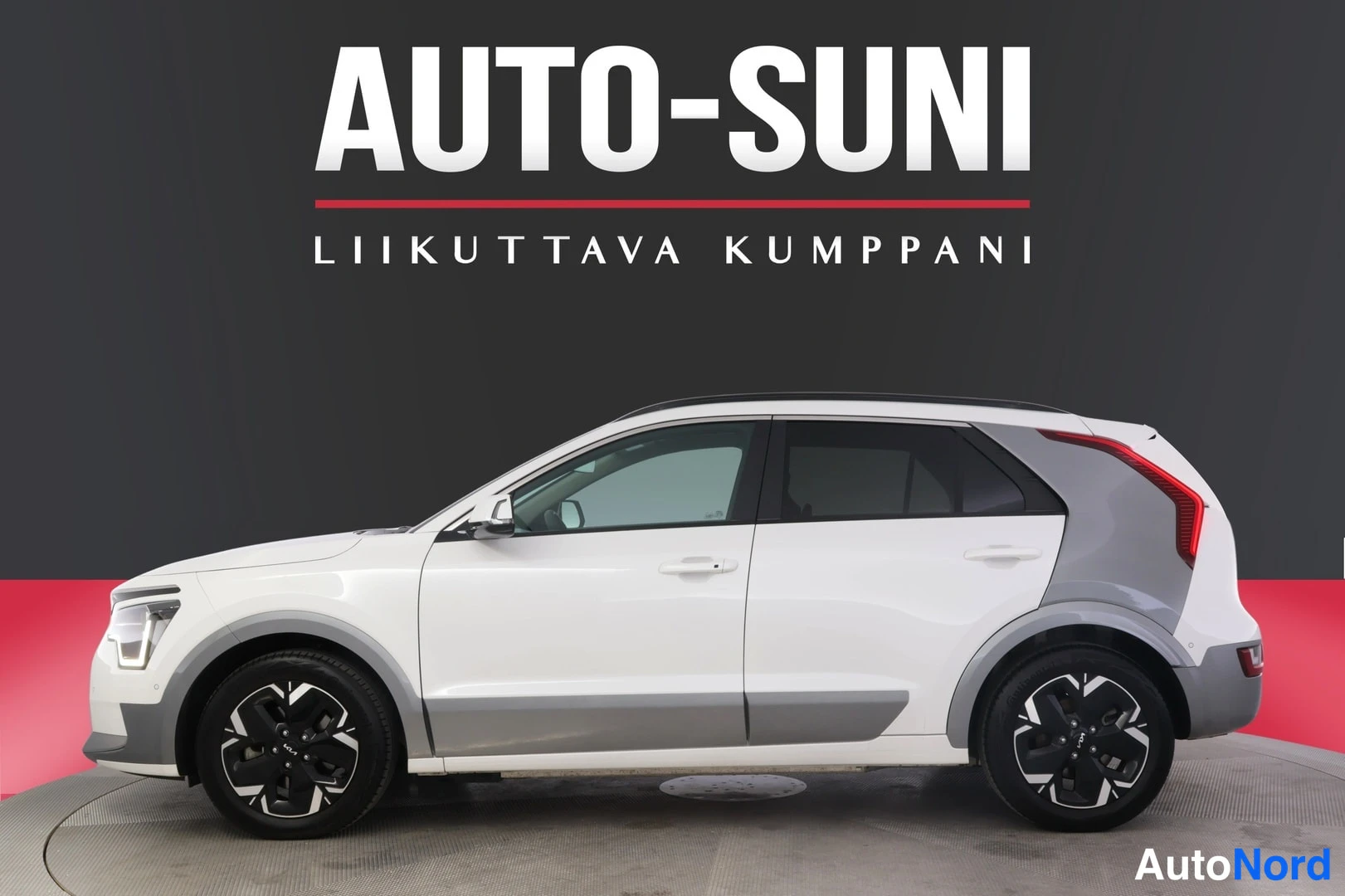 Sivulta: Autoliikkeen esittelykuva: valkoinen Kia Niro -maasturin sivuprofiili harmaata tummaa taustaa vasten. Kuvassa näkyvät tummat kevytmetallivanteet, kattokaiteet j