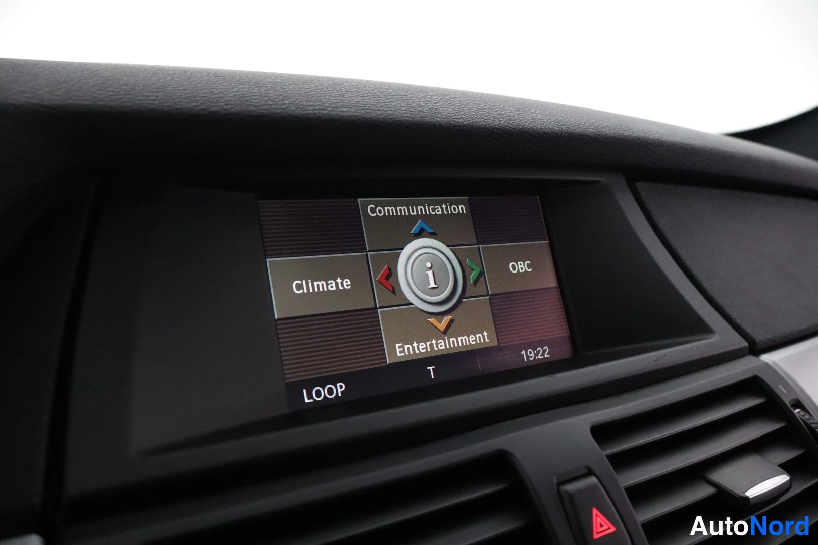 Yksityiskohta: Kojelaudan näyttö iDrive-valikossa: Communication, Climate, OBC ja Entertainment. Ajanäyttö 19:22 ja ilmastointiaukot alla.