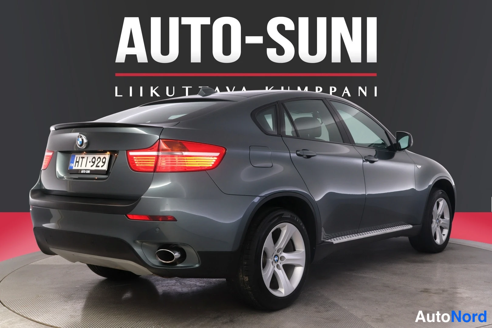Takaviisto: Takakulmakuva tummanharmaasta BMW X6:sta vasemmalta: syttyneet takavalot, rekisterikilpi, takaluukun BMW-merkki, kaksoispakoputki ja vasen kylki näkyvissä.